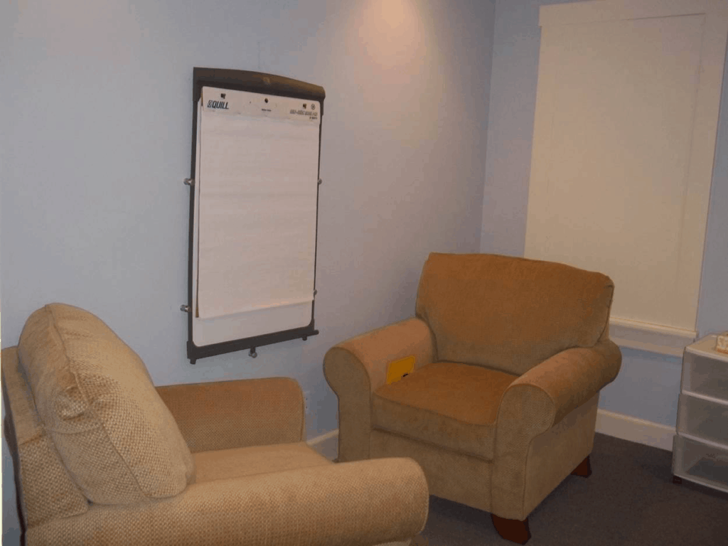 Inside the forensic interview room, with two beige armchairs near a window and an easel with paper.