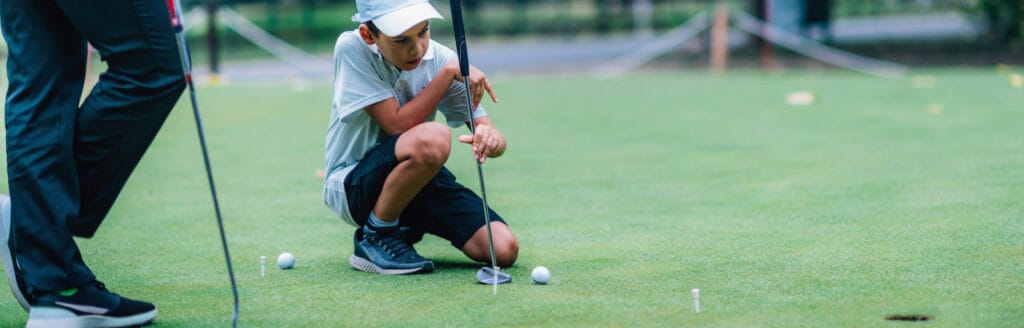 Learning Golf. Boy practicing putting with instructor